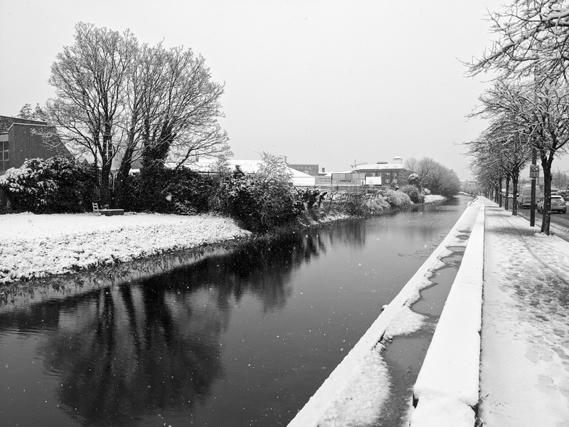The grand canal, snow flakes visible as specks against the dark of the water. Some snow on the ground along either bank.