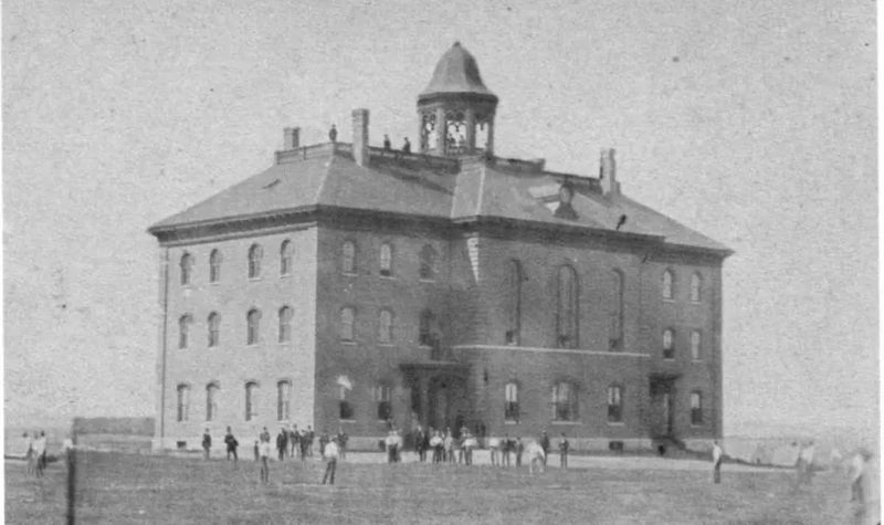 An old photograph of Founders Hall. People milling about outside and (!) on the roof.